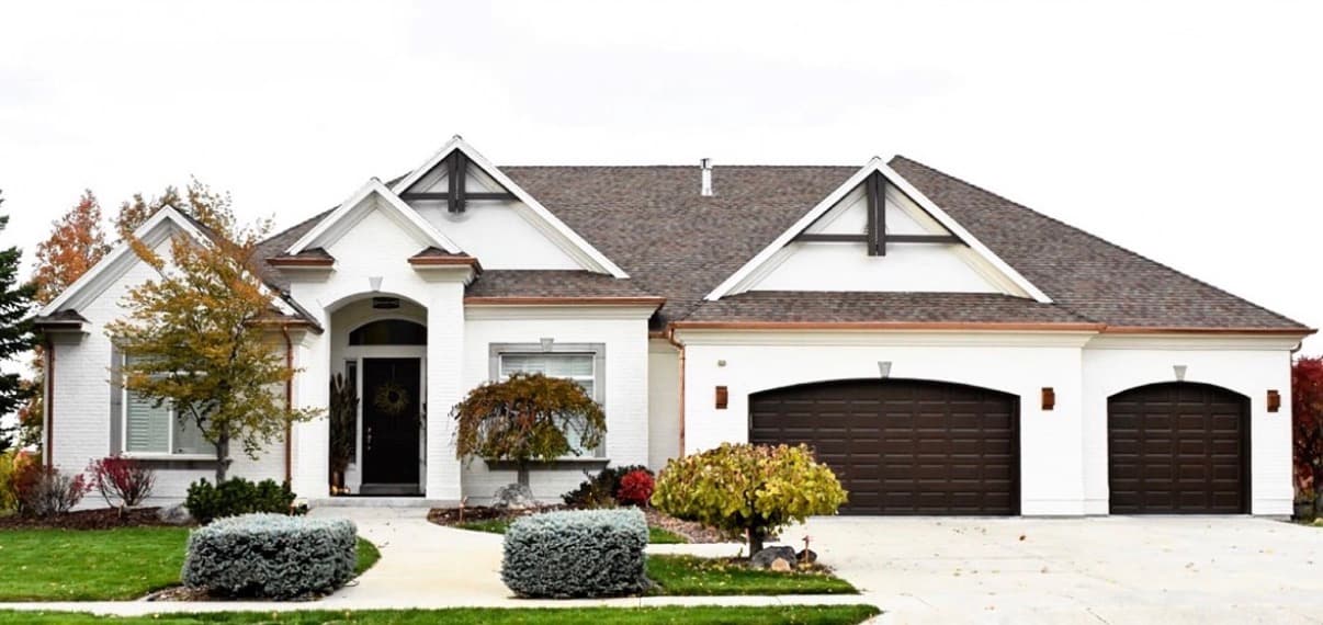A Revive-painted white brick house with dark garage doors and wood details