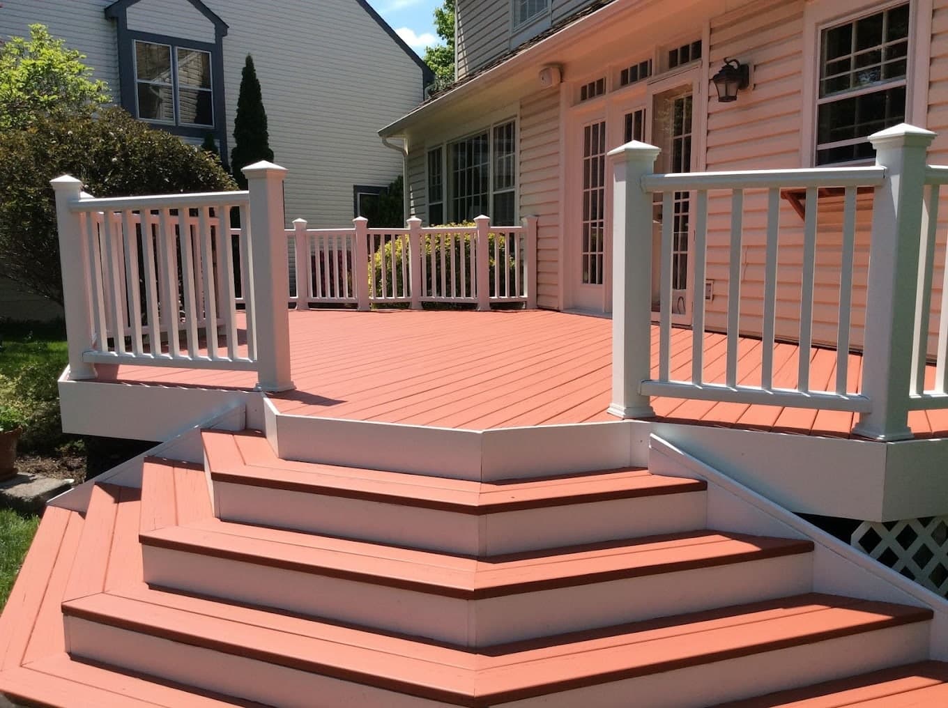 A deck stained terracotta with freshly painted white railings and steps